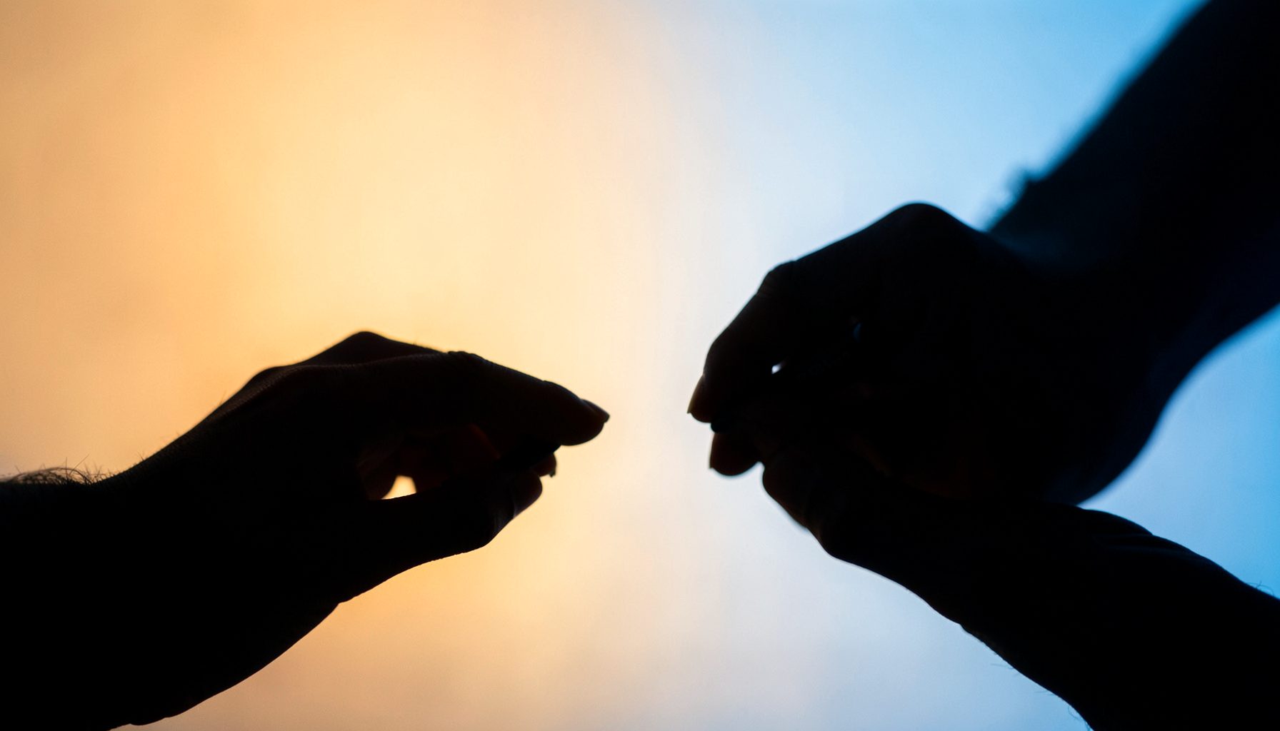 Two hands signing in silhouette against a soft gradient background of warm amber and cool blue