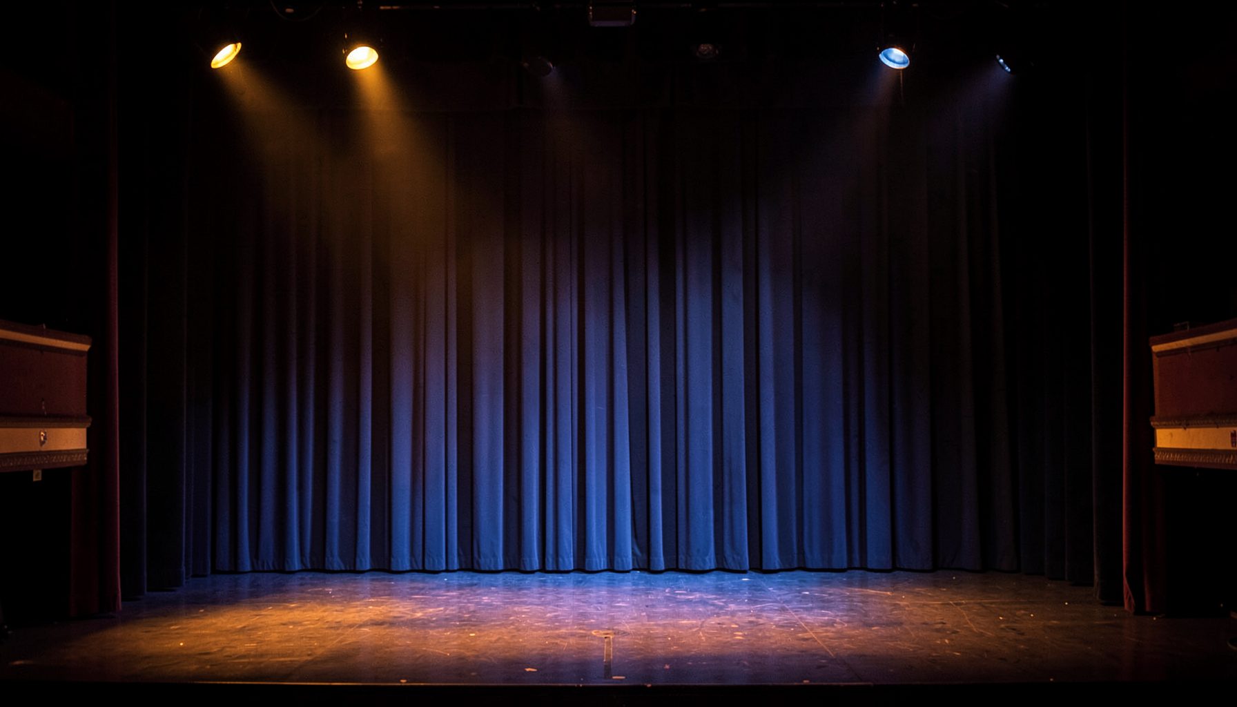 Amber and blue stage lighting across an empty theatre stage with heavy curtains